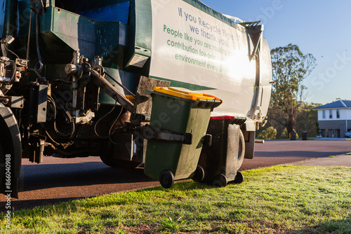 Recycling truck picking up bin from suburban roadside in morning light in Australia