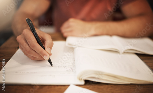 Student, hand and writing in notebook at desk for studying, learning or assignment deadline in library. University, education and person with pen for knowledge, scholarship or working on thesis