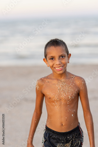 aboriginal boy on beach with sand stuck to him from where he has been playing photo