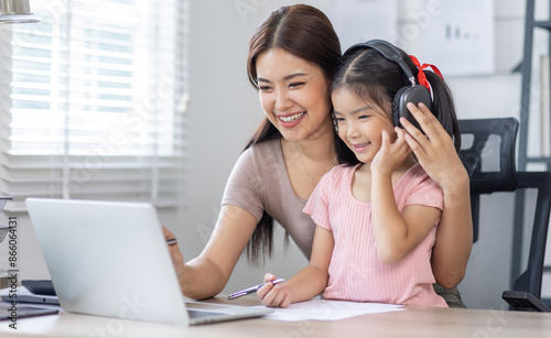 Asian business lady working on computer while her daughter hugging her