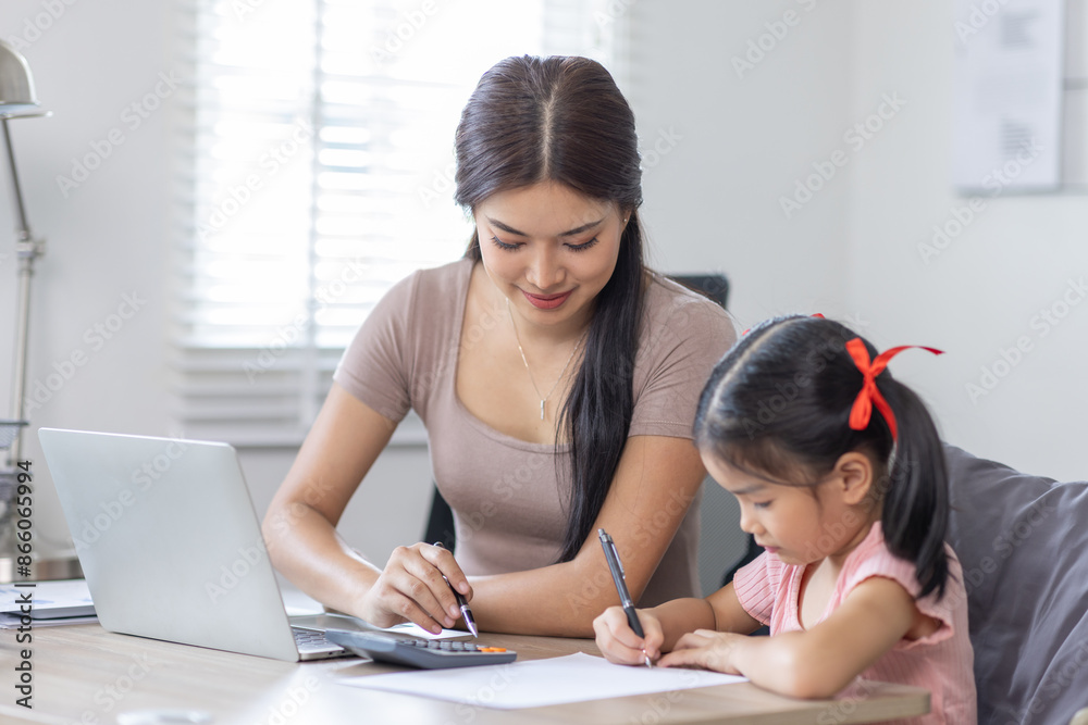 Asian business lady working on computer while her daughter hugging her