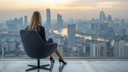 A woman in a modern office chair gazing at a sprawling cityscape through a large window at dusk image.
