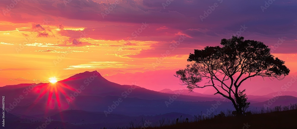 The sunset scene with tree and mountain silhouettes provides a picturesque view, ideal for a copy space image. The sunset scene with tree and mountain silhouettes provides a picturesque view, ideal for a copy space image.