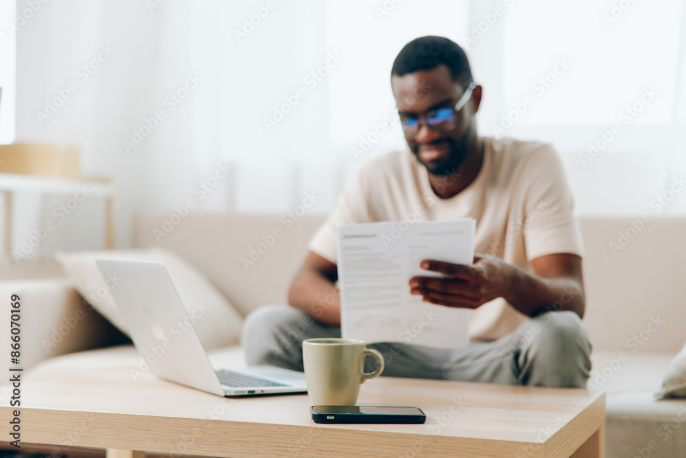 Smiling African American Man Working on Laptop in Modern Home Office Sitting on Sofa, Typing and Engaged in Cyberspace Young Millennial Freelancer Embracing Technology and Education Smiling African American Man Working on Laptop in Modern Home Office Sitting on Sofa, Typing and Engaged in Cyberspace Young Millennial Freelancer Embracing Technology and Education