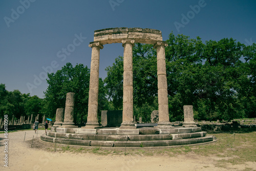 View of archeological ruins consisting of different columns or pillars taken on a sunny day in the ancient site of Olympia, Greece