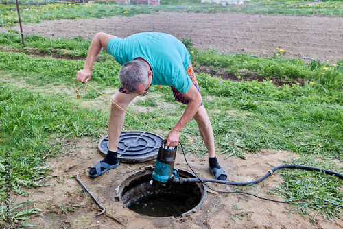 Man lowers high pressure submersible drainage pump into septic tank to pump sewage and dispose of it. photo