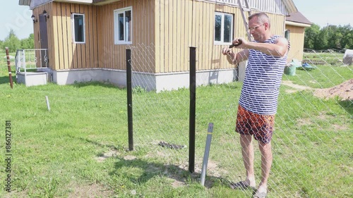 Chain-link fence is built on garden plot in nature, landowner twists ends wire of chainlink fence together.