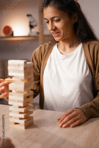 Obraz na plátně Woman smiling while playing wooden block game at home, engaging in leisure activ