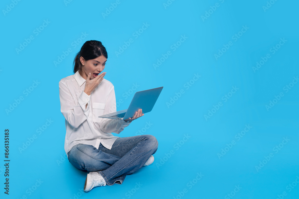 Woman Sitting on Blue Background, Looking at Laptop in Surprise Woman Sitting on Blue Background, Looking at Laptop in Surprise