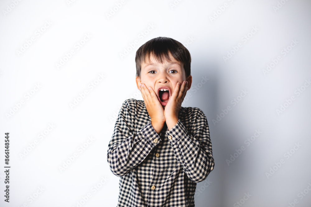 Portrait of funny young boy looking at camera with open mouth and big eyes, hands on cheek, shocked surprised expression against white background. Portrait of funny young boy looking at camera with open mouth and big eyes, hands on cheek, shocked surprised expression against white background.