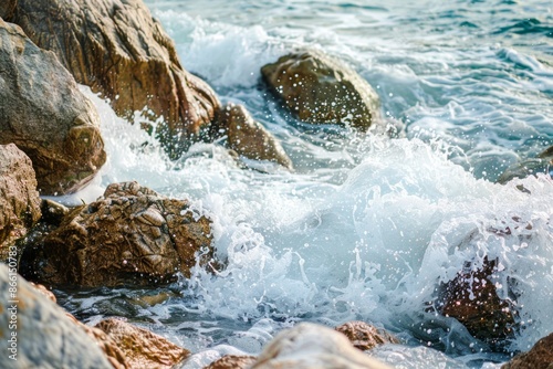 Waves crashing against rocks, with a softly blurred background of a rugged coastline and sea. 