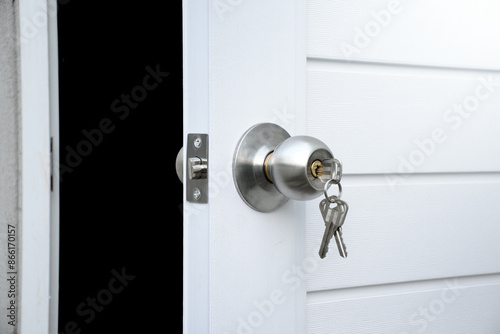 Close up open white door and silver knob with keys against gray concrete isolated on black background for concept of open the door or close the door and safety and security.