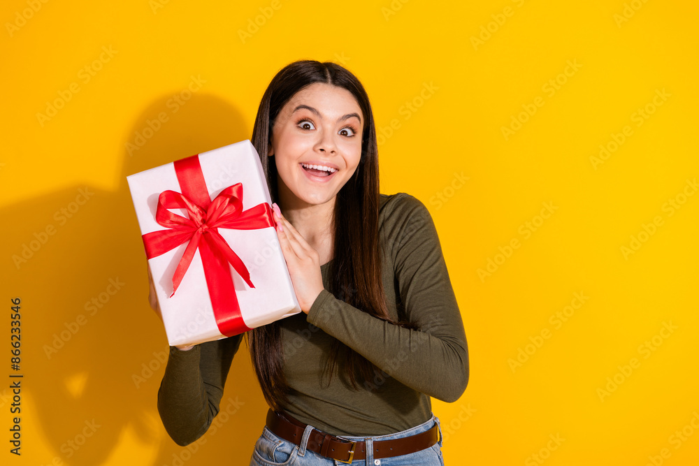 Photo portrait of lovely teen lady hold giftbox dressed stylish khaki garment isolated on yellow color background Photo portrait of lovely teen lady hold giftbox dressed stylish khaki garment isolated on yellow color background