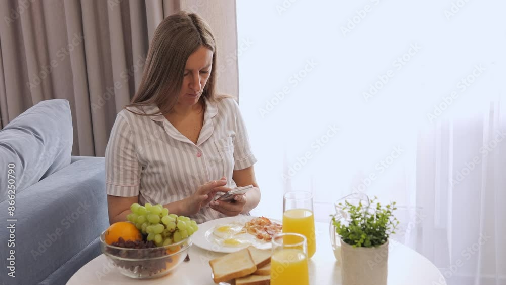 Woman reads messages on her phone while having breakfast. Phone is part of her morning, chatting with friends and getting updates. Ideal for videos about technology and everyday life from your phone. Woman reads messages on her phone while having breakfast. Phone is part of her morning, chatting with friends and getting updates. Ideal for videos about technology and everyday life from your phone.