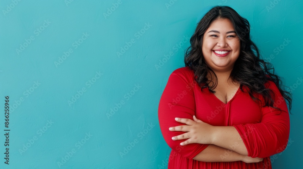 A woman with long dark hair and a red dress smiles brightly against a turquoise wall. She stands with her arms crossed, radiating confidence and joy A woman with long dark hair and a red dress smiles brightly against a turquoise wall. She stands with her arms crossed, radiating confidence and joy