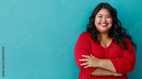 A woman with long dark hair and a red dress smiles brightly against a turquoise wall. She stands with her arms crossed, radiating confidence and joy © liliyabatyrova