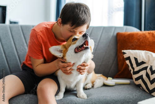 Фотография Friendly teenager with down syndrome embracing and kissing his corgi dog on comf