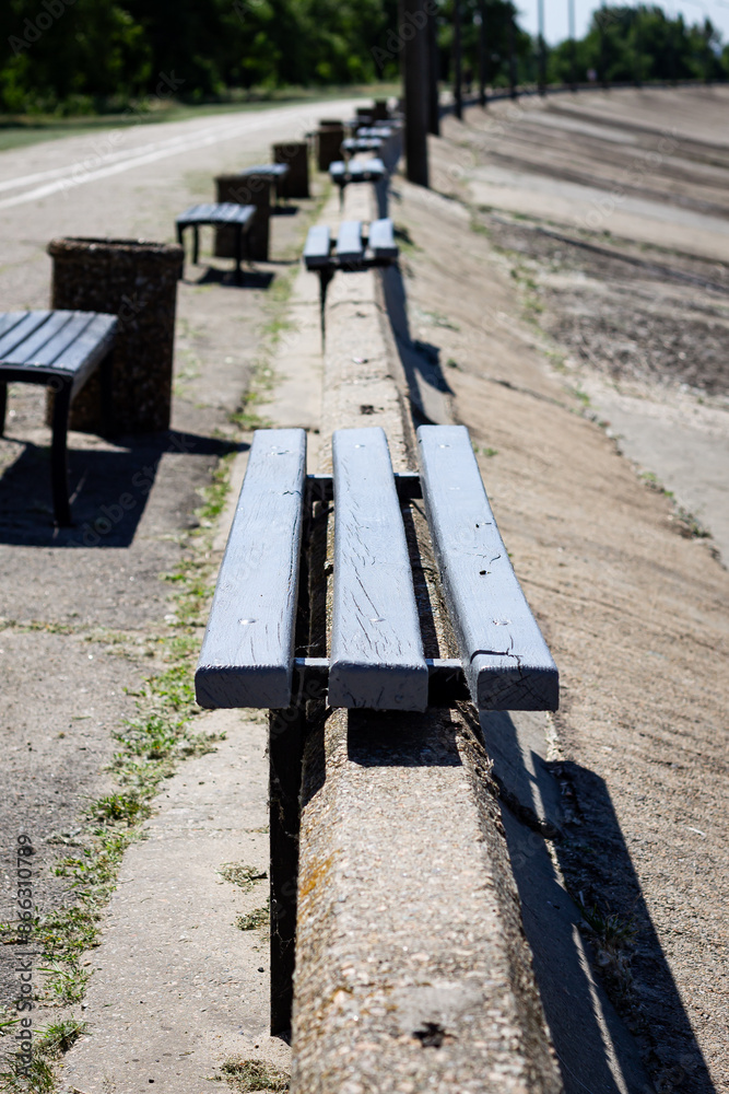 Color vertical photo of wooden benches on concrete railings on the embankment, going down to the water, on a sunny day. Color vertical photo of wooden benches on concrete railings on the embankment, going down to the water, on a sunny day.