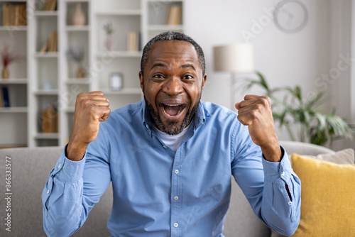 Valokuva Excited man with clenched fists celebrating success at home sitting on sofa