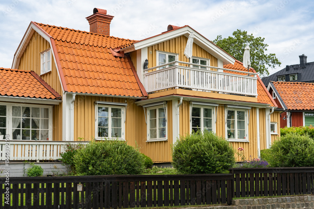 Old wooden yellow house with big balcony. Typical Swedish house surrounded by palisade fence. Beautiful wooden fence of natural wood is not painted. Ecological design. Old wooden yellow house with big balcony. Typical Swedish house surrounded by palisade fence. Beautiful wooden fence of natural wood is not painted. Ecological design.