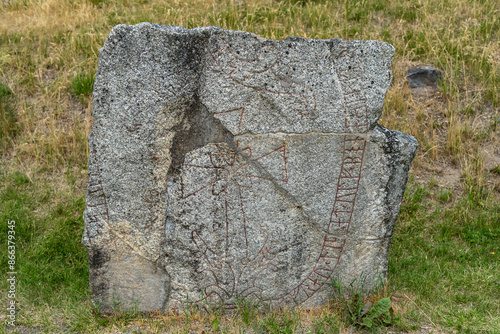 Traditional Rune stone. Old aged weathered granite gravestone in autumn. It was carved in 11th century. Ancient Big rock with runes patterns. Vikings Times. An old grave in the Sigtuna, Sweden.