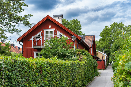 The green hedge and bushes are neatly trimmed. Old wooden red houses of past centuries in Sigtuna, ancient capital of Sweden. Two storey houses with beautiful garden design. Courtyard. 