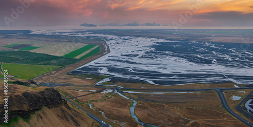 Fotografija Stunning aerial view of a vast, winding river in Iceland, surrounded by a mix of brown, green, and black terrain