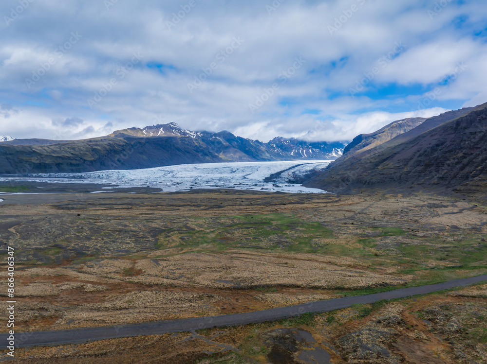 Stunning aerial view of a glacier in Iceland, surrounded by rugged mountains. A road in the foreground adds scale and perspective to the breathtaking landscape. Stunning aerial view of a glacier in Iceland, surrounded by rugged mountains. A road in the foreground adds scale and perspective to the breathtaking landscape.