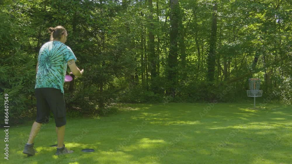 A man attempts a putt towards the basket in a wooded disc golf course, demonstrating concentration and skill in the sport A man attempts a putt towards the basket in a wooded disc golf course, demonstrating concentration and skill in the sport