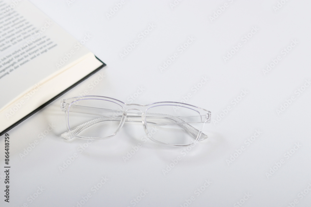 Close up of transparent glasses and an open book on white table Close up of transparent glasses and an open book on white table