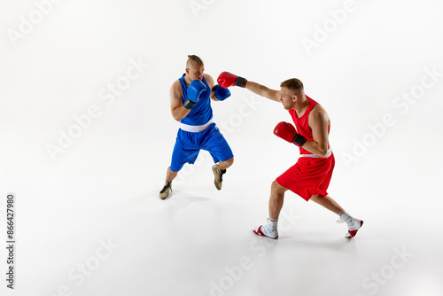 Action shot of two fighters, exchanging blows and testing their endurance in sparring session against white studio background. Concept of professional sport, healthy lifestyle, competition. Ad