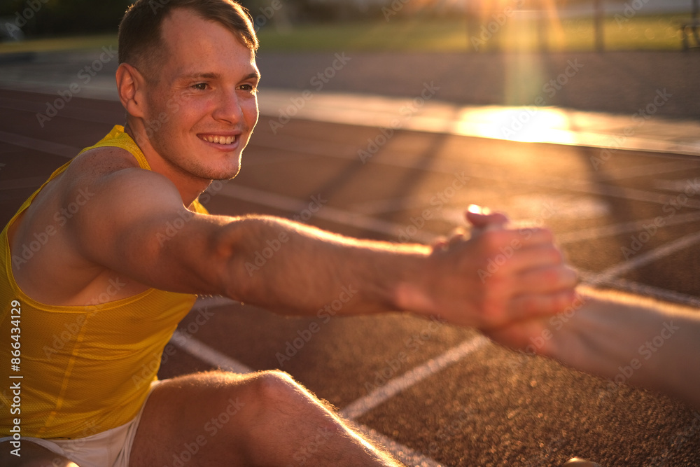 Obraz premium Two track and field athletes doing stretching on the stadium field before running
