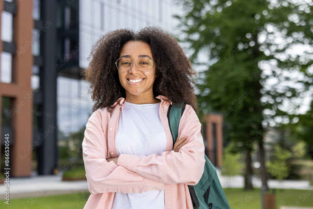Confident young female student smiling near university campus with backpack. Student wearing glasses and casual clothing standing outside modern building, showing positive and happy demeanor. Confident young female student smiling near university campus with backpack. Student wearing glasses and casual clothing standing outside modern building, showing positive and happy demeanor.