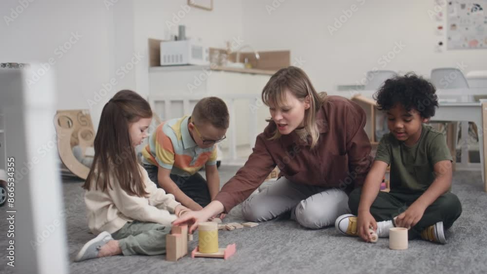 Full shot of group of diverse preschool children sitting on floor in kindergarten playing wooden toys, having competition. Caucasian female educator congratulating winner by giving handshake Full shot of group of diverse preschool children sitting on floor in kindergarten playing wooden toys, having competition. Caucasian female educator congratulating winner by giving handshake