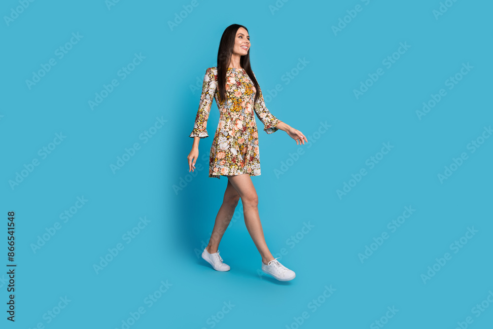 Full length photo of shiny attractive lady dressed floral print outfit looking walking empty space isolated blue color background Full length photo of shiny attractive lady dressed floral print outfit looking walking empty space isolated blue color background