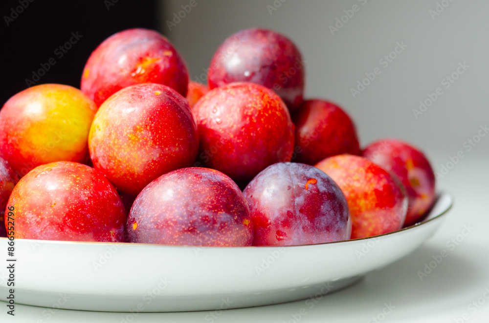 A white plate with a bunch of red plums on it A white plate with a bunch of red plums on it
