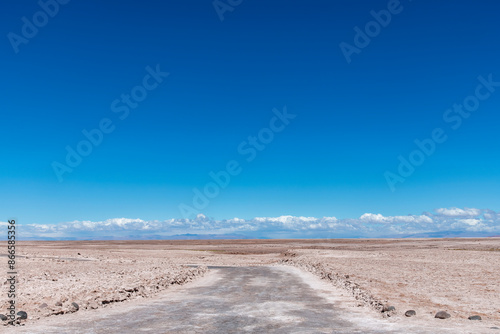 Panoramic view over dirt road along the salt flats in Atacama Desert near characteristic city San Pedro de Atacama, Antofagasta, Chile with clouds in blue sky above mountain range © Sonja