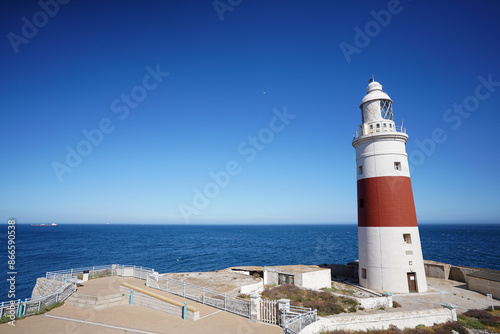 Europa Point Lighthouse facing the strait of Gibraltar on top of sea cliffs with the mountains of Morocco in the distance.