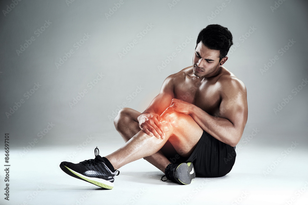 Studio, fitness and man with pain in knee, physio or cramp at gym workout for body builder training. Exercise, risk and red glow with muscle injury, overlay and ache in legs on grey background Studio, fitness and man with pain in knee, physio or cramp at gym workout for body builder training. Exercise, risk and red glow with muscle injury, overlay and ache in legs on grey background