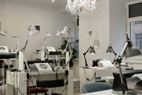 Shot of nail salon interior in modern minimalistic style with chandelier ceiling light, manicurists desks and lamps, copy space