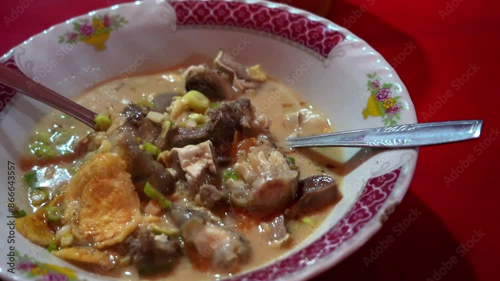 A person ladles a steaming bowl of Indonesian lamb soup or Sop Kambing Betawi at the street food restaurant. A person ladles a steaming bowl of Indonesian lamb soup or Sop Kambing Betawi at the street food restaurant.