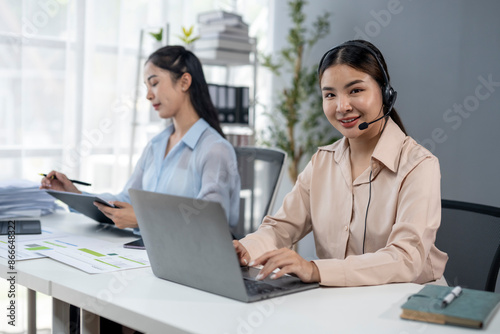 Two women are sitting at a desk with a laptop and a book © Wasana