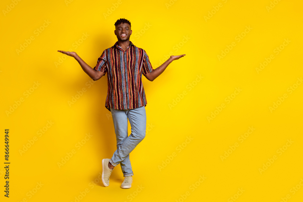 Full size photo of nice young man hold empty space vs wear shirt isolated on yellow color background Full size photo of nice young man hold empty space vs wear shirt isolated on yellow color background