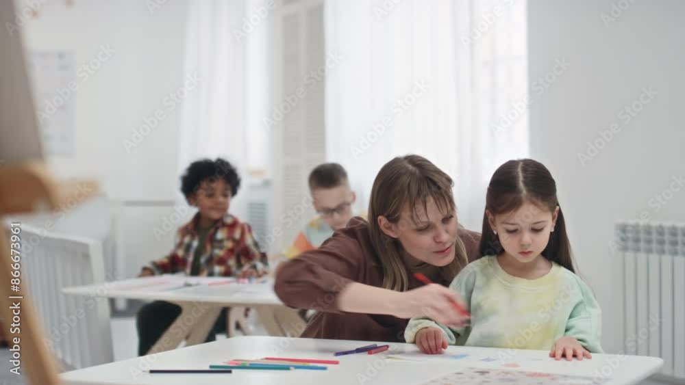 Medium shot of young Caucasian woman teaching preschool kids during art lesson in kindergarten, helping individually and assisting drawing process Medium shot of young Caucasian woman teaching preschool kids during art lesson in kindergarten, helping individually and assisting drawing process