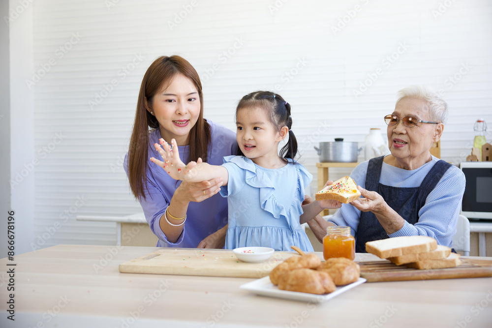 cute playful little girl putting orange jam and topping candy on bread toast beside mother and grandmother in the kitchen cute playful little girl putting orange jam and topping candy on bread toast beside mother and grandmother in the kitchen