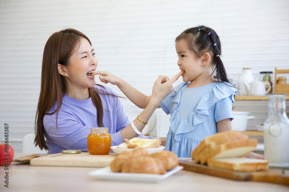 mother tasting orange jam with her daughter in the kitchen mother tasting orange jam with her daughter in the kitchen