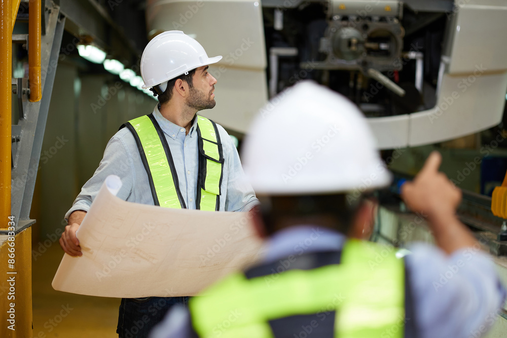 Worker or engineer using theodolite surveying optical instrument and coworker holding blueprint paper at construction train station Worker or engineer using theodolite surveying optical instrument and coworker holding blueprint paper at construction train station