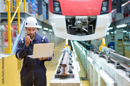 Engineer or worker working on laptop computer and talking on walkie talkie at construction train station