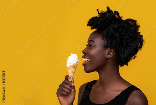 Happy black teenage girl eating cone ice cream, smiling on yellow background with copy space