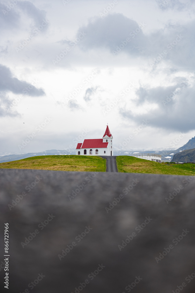 Stunning view of the Ingjaldshólskirkja, a historic little red-roofed church located in Snæfellsnes penisula, A nice road leads down and back up a hill with great views of the mountains.
